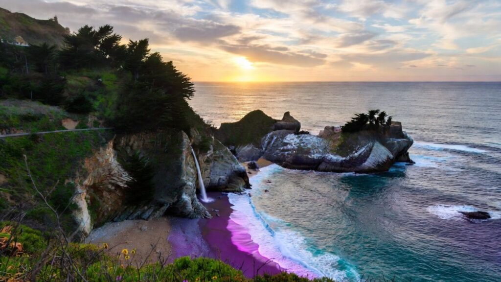 Dramatic spring sunset at Big Sur, California – McWay Falls cascades onto a purple sand beach as the Pacific Ocean glows in golden light
